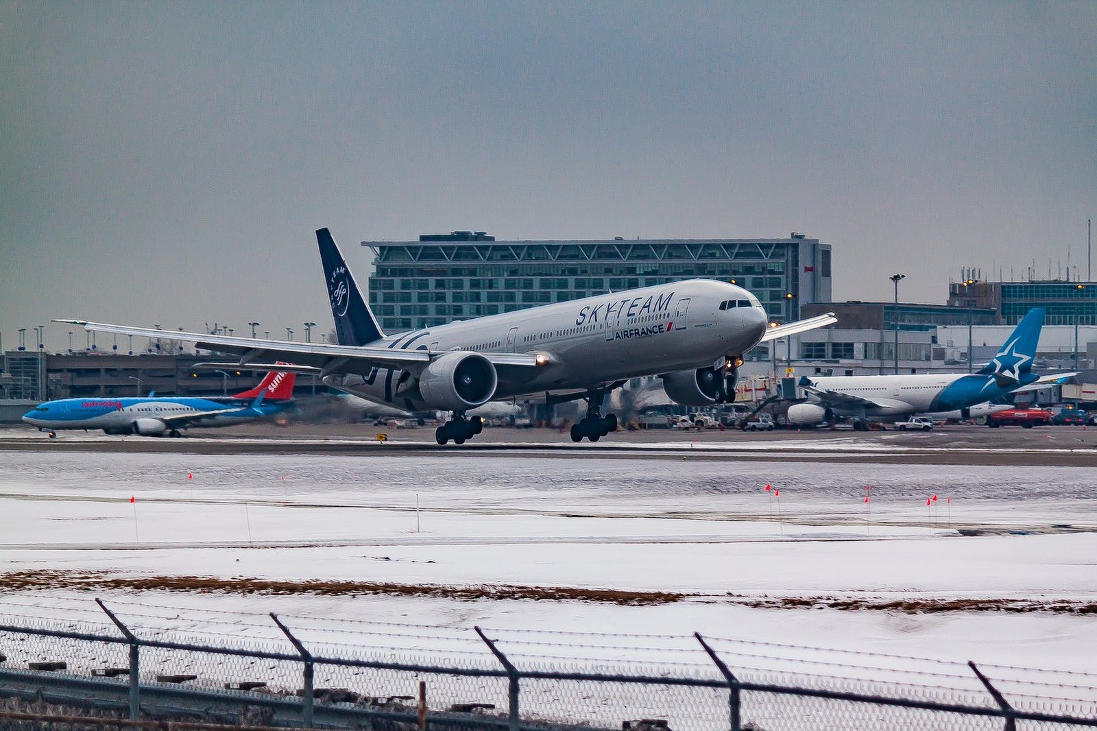 aircraft flying over runway near airport building